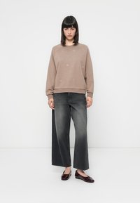 Sweatshirt marron clair avec un col rond et des détails embellis, associé à un pantalon en jean gris large et des mocassins en vernis bordeaux.