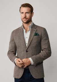 Blazer a quadri marrone con un design strutturato, dotato di un solo bottone, rever a punta e una tasca verde. Dettagli in tessuto testurizzato.