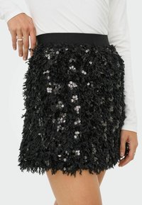 Zwarte paillettenrok met een textuurrijke, pluizige stof waarin pailletten verspreid zijn. Elastische tailleband voor pasvorm en comfort.