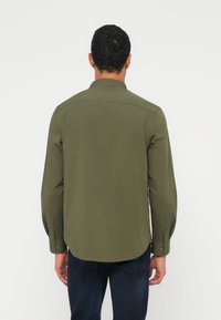 Παντελόνι πράσινου ελιάς με μακρύ μανί�κι, γιακά με κουμπιά, πλευρικές σχισμές και διακοσμητικά κουμπιά στα μανίκια, κατασκευασμένο από υφή υφάσματος λεία.