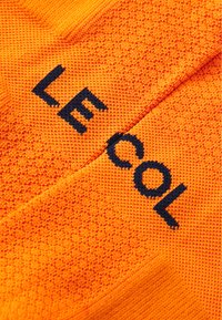 Maglia ciclistica arancione brillante con tessuto strutturato. Presenta una scritta in blu audace "LE COL". Il design include una forma aderente e senza cuciture.