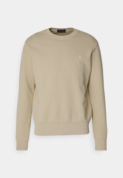 Beige huppari, joka on valmistettu puuvillasekoitteesta, jossa on pyöreä kaula-auko, ribbikudin hihansuut ja helma, sekä pieni brodeerattu logo vasemmassa rinnassa.