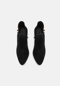 Schwarze Wildleder-Ankle-Boots mit Absatz und spitzem Schuhbereich, ausgestattet mit einem goldfarbenen Akzent an der Seite und einer glatten Textur.