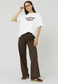 T-shirt blanche avec "HAMPTON GROVE" imprimé en bordeaux, associée à un pantalon à rayures marron et des baskets bordeaux à lacets.