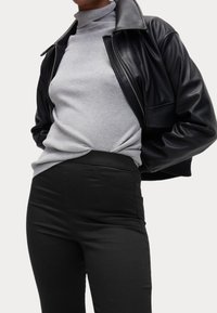 Sort læderjakke med bred krave, iført over en lys grå ribbet turtleneck og højtaljede sorte bukser. Glatte teksturer og tætsiddende design.