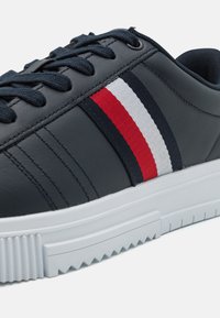 Sneaker in pelle blu navy con suola in gomma bianca. Presenta un design a strisce rosse, bianche e blu navy sul lato e lacci texturizzati.