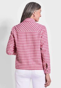 Pinke und weiße karierte Jacke mit Kragen, langen Ärmeln und seitlichen Schlitzen. Der Stoff wirkt weich. Weiße Jeans werden als Unterteil getragen.