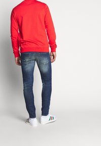 Červená mikina, modré skinny džíny s vybledlým efektem a bílé tenisky se zelenými, červenými a černými pruhy.