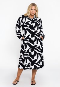 Schwarz-weißes langes Hemdkleid mit Blättermuster, featuring eine Knopfleiste, lange Ärmel und Seitentaschen. Glatte Stofftextur.