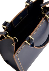 Navyblaue Lederhandtasche mit tanfarbenen Akzenten, goldenen Beschlägen und offenem Top. Sie verfügt über eine strukturierte Außenseite und eine Innenstasche.