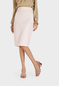 Falda lápiz de longitud a la rodilla en rosa claro con bolsillos laterales, combinada con sandalias de tacón plateadas metálicas con correas decorativas y punta abierta.