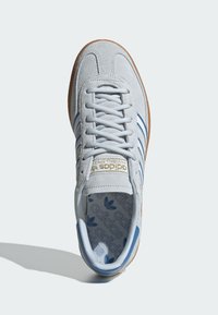 Pelēki zamša sporta apavi ar zilām svītrām; komplektā baltas auklas un gumijas zoles. Iekšpuses dizainā ir atkārtots zils adidas logo. 