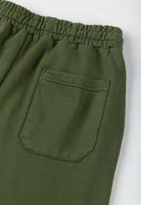 Zielone dresy wykonane z miękkiego materiału, z elastycznym pasem w talii i jedną tylną kieszenią z naszytym prostokątnym klapkiem.