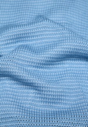 Light blue knitted fabric with a textured waffle pattern, showing gentle folds and soft material details.