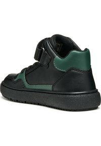 Baskets montantes en cuir noir avec accents verts, comportant une sangle Velcro et une semelle en caoutchouc texturé pour une adhérence accrue.