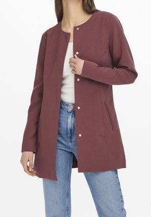 Burgundy lightweight jacket with a round neckline, snap closures, and side pocket. Smooth texture, tailored fit, paired with blue jeans.