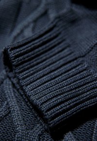 Dunkelblauer gestrickter Pullover mit Rippbündchen. Verfügt über ein strukturiertes Muster und weichen Stoff. Fokus auf Nahaufnahme der Strickdetails.