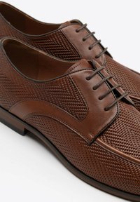 Zapatos de cuero marrón con parte superior de malla texturizada, puntera redonda y diseño tradicional con cordones. Presentan costuras en contraste y una suela resistente.