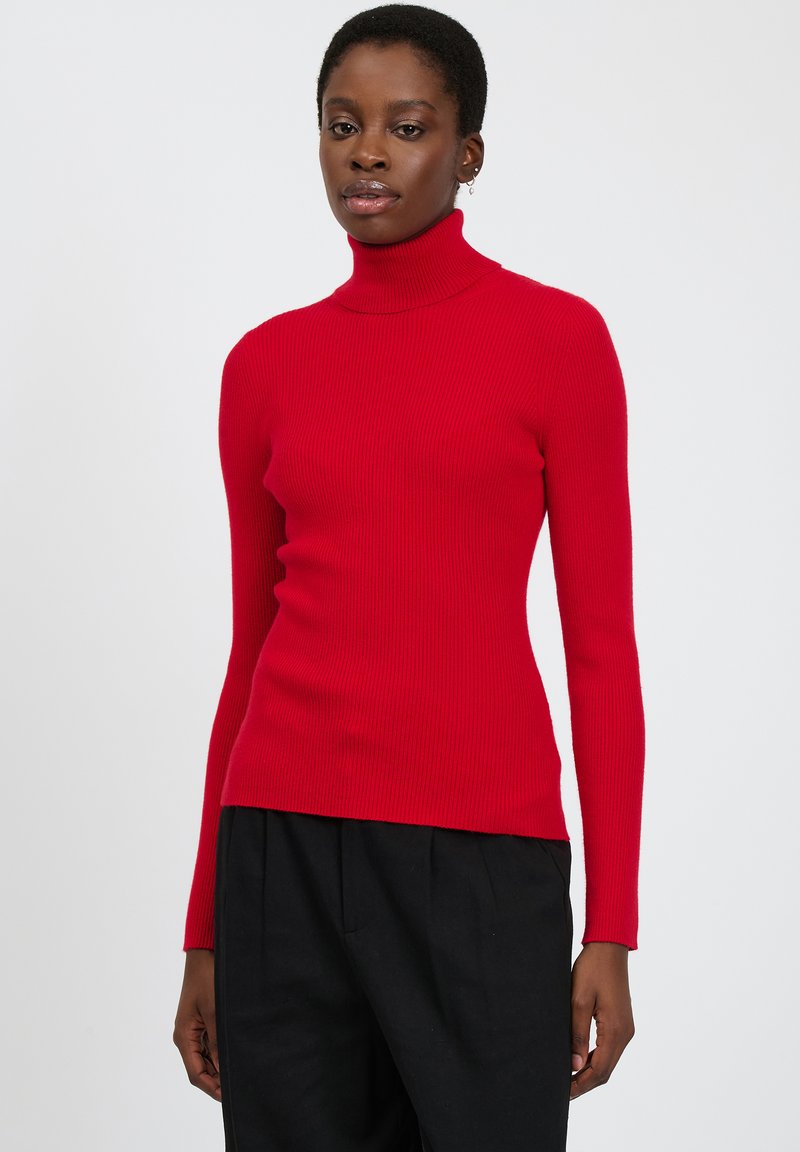 Maglione a collo alto rosso a coste con maniche lunghe, design aderente e texture morbida, abbinato a pantaloni neri.
