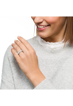 Silberner Ring mit strukturierten Oberfläche, getragen an einer Hand. Die Person trägt einen hellgrauen Pullover mit einem gerüschten Kragen darunter.