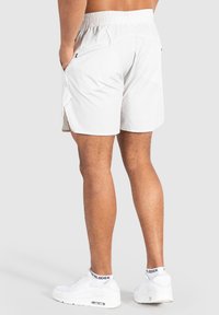 Pantalones cortos deportivos blancos con una cinturilla elástica texturizada, bolsillos laterales y un dobladillo ligeramente curvado. Se llevan con zapatillas blancas y calcetines.