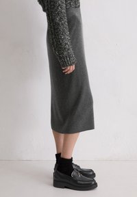 Jupe midi en tricot grise avec une taille ajustée, associée à des mocassins noirs et des chaussettes en tricot, mettant en avant une texture douce et un design épuré.