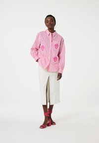 Striped pink and white button-up jacket with heart embroidery, paired with a white skirt featuring a front slit and pink heeled sandals.