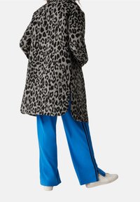 Leopardmönstrad fuskpälskappa med sidoflikar, kombinerad med ljusblå träningsoverallsbyxor med svarta ränder och vita sneakers.