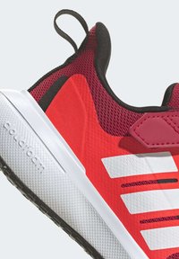 Červená sportovní bota s prodyšným svrškem a černými detaily, strukturovaná bílá podrážka a logo na boku; obsahuje úchyt pro snadné obutí.