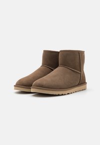 Bottes chevilles en daim marron avec un bout arrondi, des détails de couture minimalistes et une semelle en caoutchouc marron clair présentant un motif texturé.