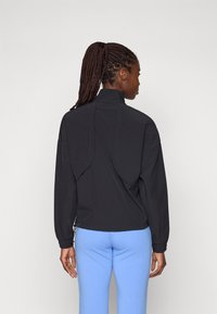Black pullover jacket with a high collar, featuring dropped shoulders and a perforated back detail. Paired with light blue leggings.