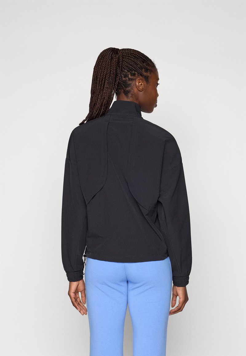 Black pullover jacket with a high collar, featuring dropped shoulders and a perforated back detail. Paired with light blue leggings.