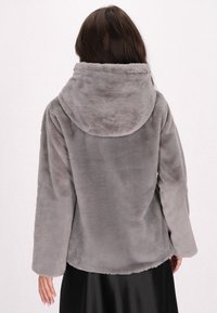 Grå, plysset faux fur-jakke med en stor hætte, lange ærmer og en løs pasform, der har en blød tekstur. Ingen synlige lukninger eller mønstre.