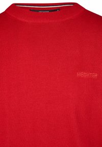 Roter, gerippter Pullover mit einem Stehkragen und subtil gesticktem Logo auf der Vorderseite. Hergestellt aus einem weichen Strickmaterial.
