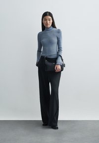 Pelēkā svītrainā garajai piedurknēm turtlenecka, melnie platā uzvalka bikses, mazs melns rokassomas ar siksniņu, gluda tekstūra, minimāli piederumi, tīras līnijas.