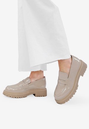 Mocasines de charol beige con suela gruesa, que cuentan con una textura suave y un sutil detalle de correa en la parte superior.