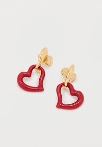 Κρεμαστά σκουλαρίκια σε σχήμα κόκκινης καρδιάς με γυαλιστερό φινίρισμα, μεταλλικά στοιχεία σε χρυσό τόνο και ασφαλή κουμπώματα καρφίτσας. Η υφή της επιφάνειας προσθέτει οπτικό ενδιαφέρον.