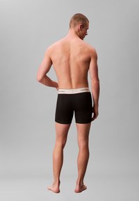 Svarta boxershorts med ett vitt Calvin Klein-midjeband, som visar en slät textur och åtsittande design, sedd bakifrån med bar hud synlig.