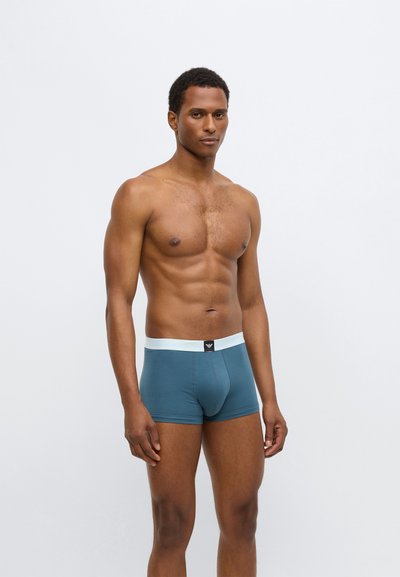 Vyriški boksininkų šortai turkio spalvos audinyje, su balta juosmens juosta ir juoda etikete. Lygus audinys, prigludęs dizainas, siekiantis viduriniąją šlaunies dalį.