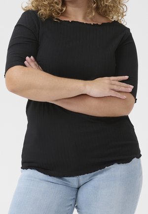 Zwart geribbeld topje met een golvende halslijn en korte mouwen, gecombineerd met lichtblauwe jeans. De stof heeft een gladde textuur en een aansluitend ontwerp.