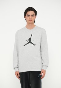Grauer Langarm-Sweatshirt mit schwarzem "Jumpman"-Logo und "A R"-Text. Der Stoff scheint weich zu sein, mit einem Rundhalsausschnitt und lockerer Passform.