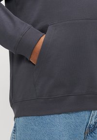 Σκούρο μπλε ναυτικό φούτερ με τσέπη καγκουρό, ριμπ μανσέτες και λεία υφή, συνδυασμένο με ανοιχτό μπλε τζιν παντελόνι.