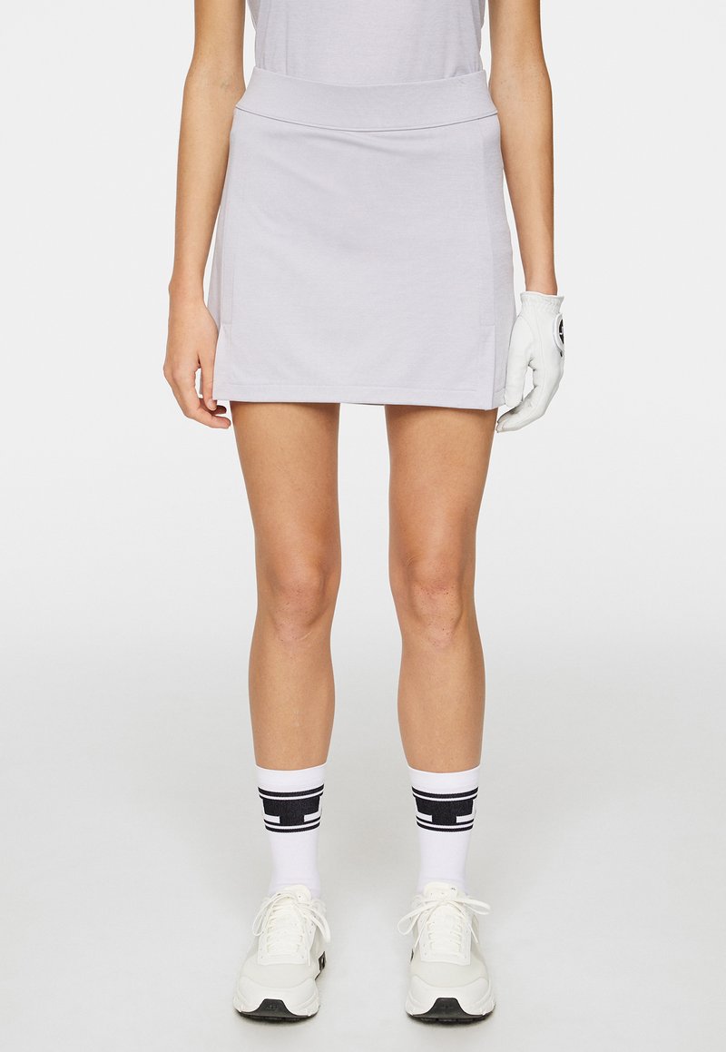 Ljusgrå idrottskjol med en slät textur, bred midjeband och sidofickor, kombinerad med vita strumpor med svarta ränder och vita sneakers.