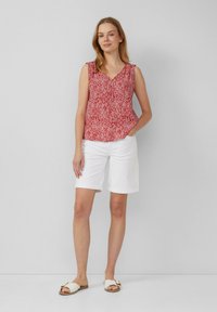 Rode mouwloze top met een geometrisch patroon, gecombineerd met witte shorts en platte witte sandalen. Eenvoudig design, relaxte pasvorm, casual zomerse look.
