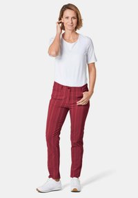 Witte short-sleeve shirt met ronde hals, gecombineerd met strakke rode gestreepte broek. Schoeisel bestaat uit witte sneakers met een rubberen zool.