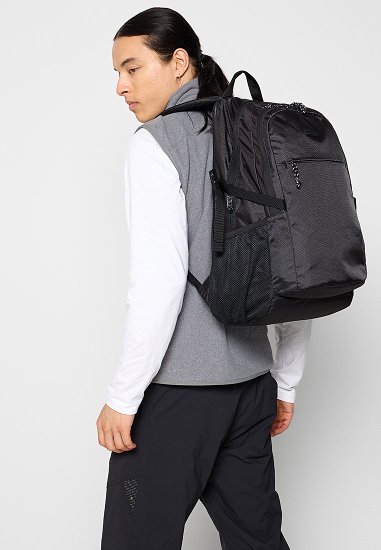 Zwarte nylon rugzak met een gestructureerde oppervlakte, een voorvak en gaas zijvakken. Verstelbare banden en een gewatteerde rug voor comfort.