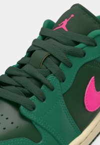Sneaker verde em couro com o logótipo rosa da Air Jordan na lingueta. Possui atacadores verdes, biqueira perfurada e sola em borracha bege.