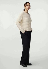 Cremfarbener, gestrickter Cardigan mit einem Kabelmuster, runden Ausschnitt und Knopfverschluss, kombiniert mit schwarzen, geraden Hosen.