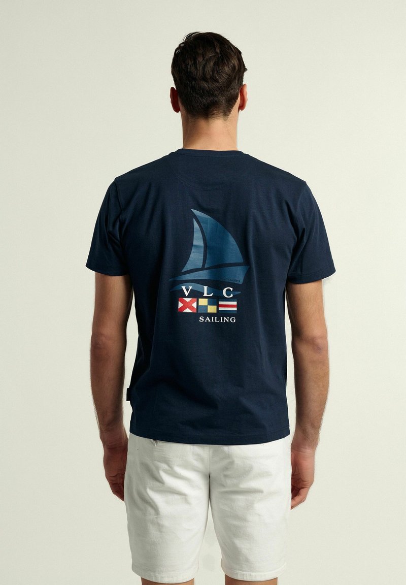 Camiseta de algodón azul marino con un gráfico de un velero, "VLC," y banderas, con letras blancas que dicen "NAVEGACIÓN" en la parte inferior.