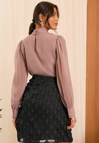 Blusa rosa chiaro con maniche a sbuffo, dettagli con bottoni sulla schiena, abbinata a una gonna nera con un motivo floreale testurizzato.